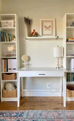 a white desk with books and baskets on it in a living room area next to a wall mounted bookcase