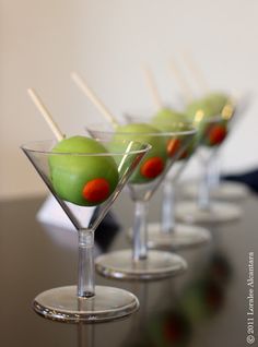 four martini glasses with green olives in them