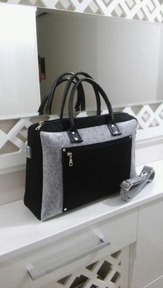 a black and grey purse sitting on top of a white counter next to a mirror