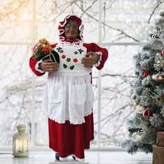 a woman dressed in red and white standing next to a christmas tree wearing an apron