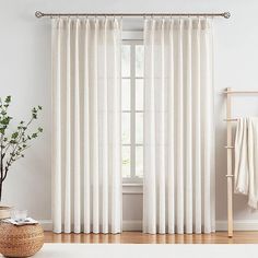 a white curtain hanging in front of a window next to a wooden chair and potted plant