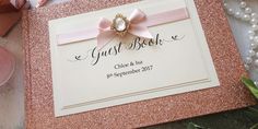 a pink and gold wedding guest book with a bow on it, surrounded by flowers