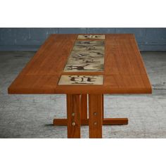 a wooden table with four different designs on it's top and two legs, in front of a gray wall