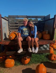 a man and woman sitting on a wooden bench surrounded by pumpkins