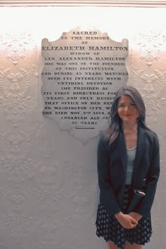 a woman standing in front of a plaque with words on it and wearing a skirt