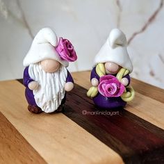 two little gnomes with flowers sitting on a wooden table next to each other in front of a marble wall