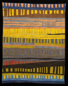 a colorful quilt hanging on the wall in front of a black background with an orange, yellow and blue design