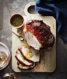 sliced pork on a cutting board with wine glasses and utensils next to it