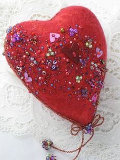 a red heart shaped pillow sitting on top of a white lace covered tablecloth next to a necklace