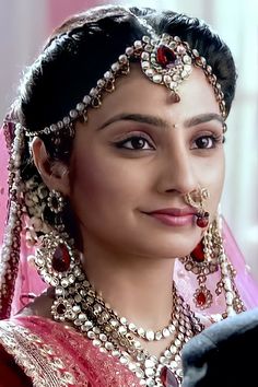 a woman in a red and gold bridal outfit with jewelry on her head, looking at the camera