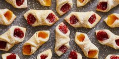 small pastries are arranged on a silver tray with powdered sugar and jelly toppings