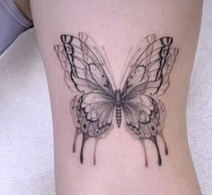 a small butterfly tattoo on the side of a woman's leg, it is black and white