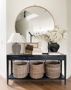 a black table with baskets and a mirror on the wall next to it, in front of a staircase