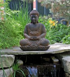 a buddha statue sitting on top of a stone slab next to a small waterfall in a garden