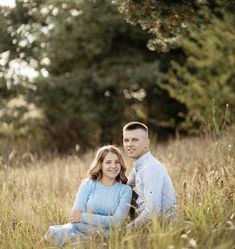 a man and woman are sitting in the tall grass with their arms around each other