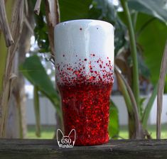 a red and white cup sitting on top of a wooden table next to a plant