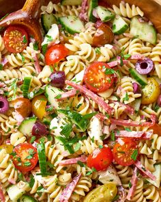 a pasta salad with tomatoes, cucumbers, olives and onions in a wooden bowl