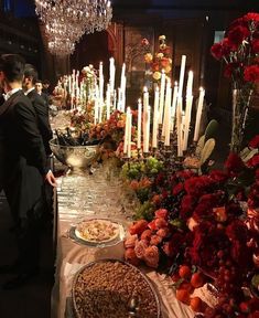 a buffet table with candles and food on it, surrounded by red flowers in vases