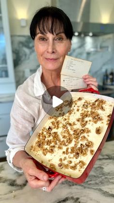 a woman holding a pan filled with food on top of a kitchen counter next to an envelope