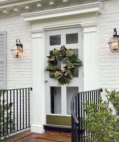 a wreath is hanging on the front door of a white brick house with wrought iron railings