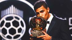 a man holding an award in front of a soccer ball and trophy on a stage