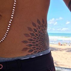 a woman's stomach with a flower tattoo on the side and an ocean in the background