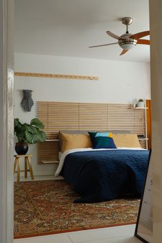 a bedroom with a bed, ceiling fan and wooden slatted headboard on the wall