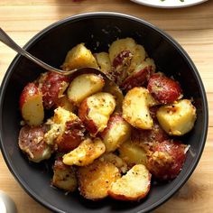 a black bowl filled with potatoes and meat on top of a wooden table next to a fork