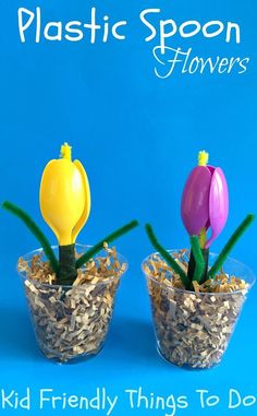 two plastic flowers sitting in small glass vases filled with dirt and grass on a blue background