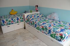 two children's beds in a room with blue walls and white drawers, one has a toy elephant on top of the bed