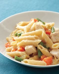 a white bowl filled with pasta and vegetables on top of a blue table cloth next to a fork