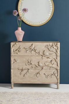 a vase with flowers sitting on top of a dresser next to a mirror and blue wall