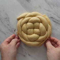 two hands are holding a pastry dough in the shape of a flower on a marble surface