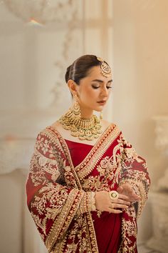 a woman wearing a red and gold bridal outfit with jewelry on her neck, standing in front of a white wall