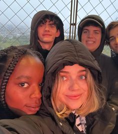 four young people posing for a photo in front of a fence with the city behind them