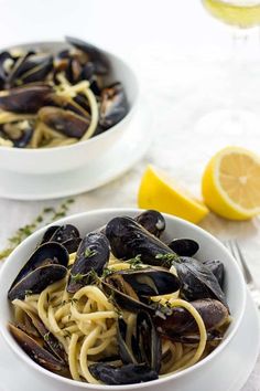 two bowls filled with pasta and mussels on top of a table next to lemon wedges