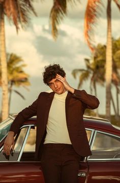 a man leaning on the door of a car with palm trees in the back ground