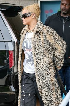 a woman in leopard print coat and black jeans walking towards a car with another man behind her