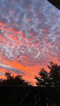 an airplane flying in the sky at sunset with clouds and trees behind it, as seen from a deck