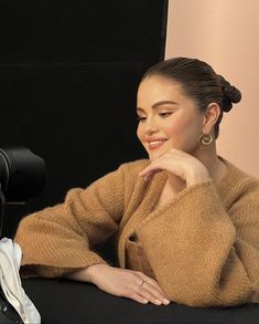 a woman sitting in front of a camera with her hand on her chin and looking at the camera