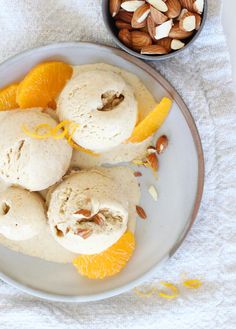 an orange gelato with almonds and orange slices on a plate next to a bowl of nuts