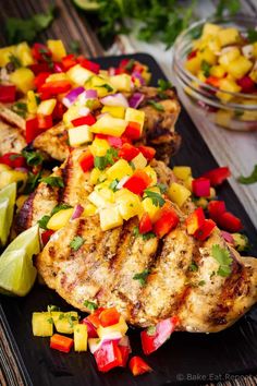 grilled chicken with pineapple salsa and lime wedges on a black platter