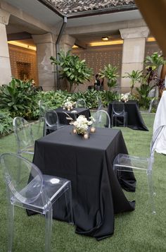 the tables are set up with clear chairs and black tablecloths for an elegant event