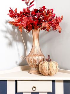 a vase filled with red flowers sitting on top of a white table next to a pumpkin