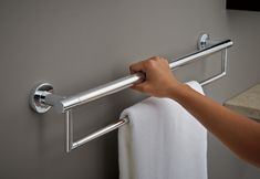 a person holding onto a towel bar in a bathroom with grey walls and white towels