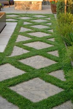 a stone walkway with grass in the middle and potted plants on either side, leading to an outdoor seating area