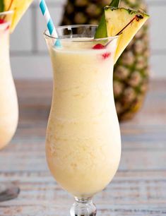 two glasses filled with pineapple milkshakes on a table next to each other