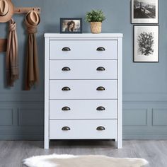 a white chest of drawers in a room with pictures on the wall and a sheepskin rug