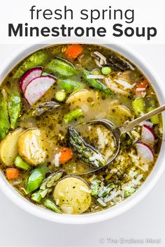 a white bowl filled with soup and vegetables on top of a table next to a spoon