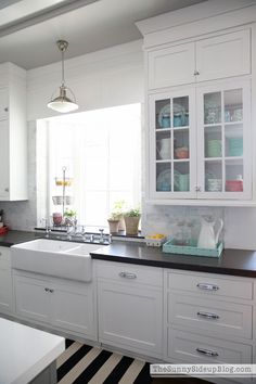 a kitchen with white cabinets and black counter tops is pictured in this image, there are flowers on the window sill